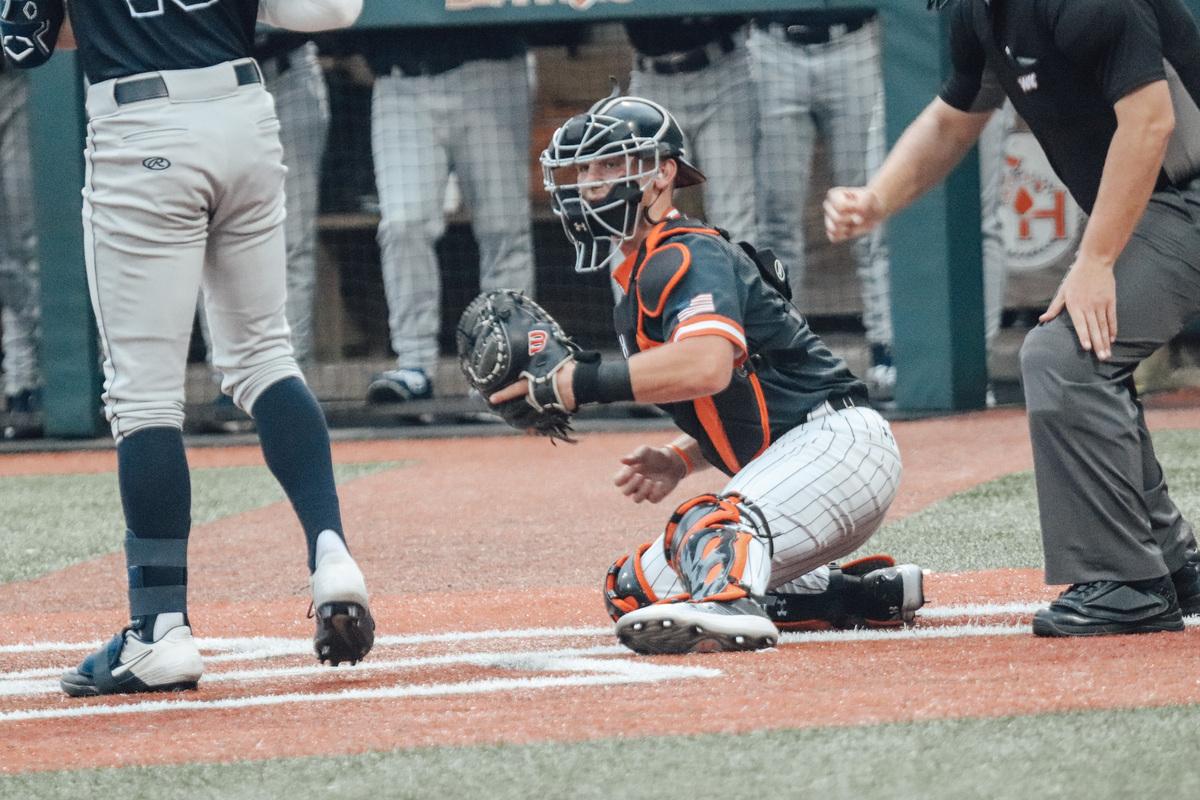 Focused and ready, the catcher takes his position behind the plate, glove at the ready and eyes scanning the field as he prepares to receive the pitch and defend his team's home plate.